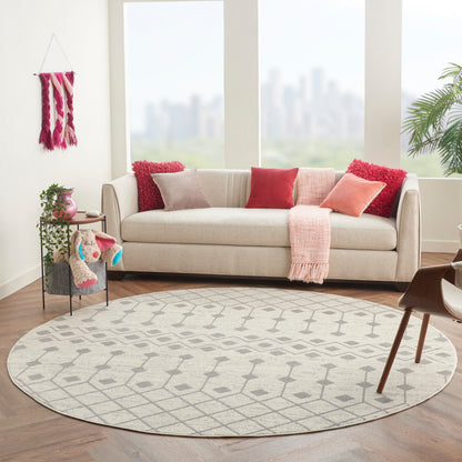 8' round bohemian geometric rug in a sunlit living room with a beige fabric sofa, pink accents, and houseplants.