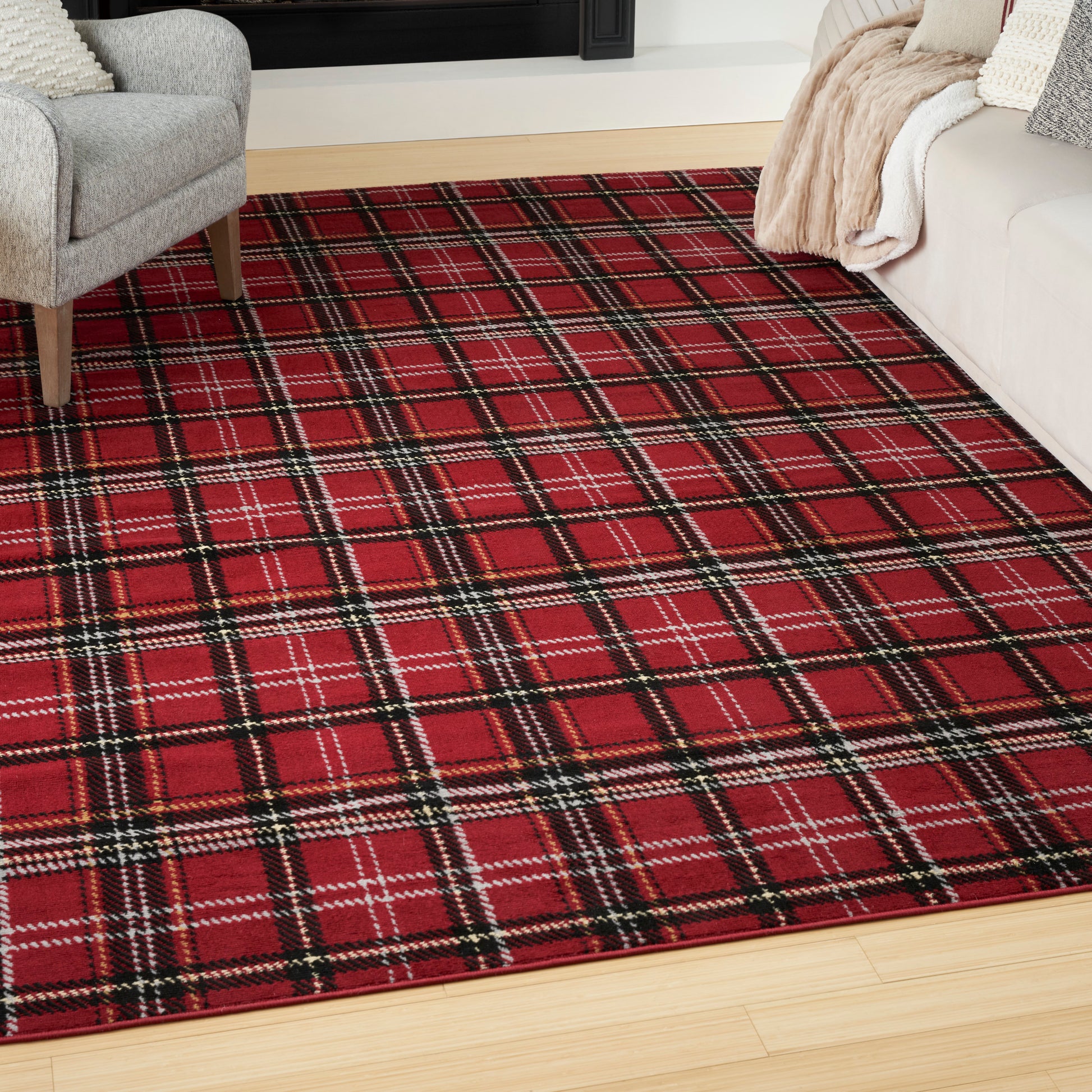 Red plaid area rug with black & white lines on light wood floor, living room corner with gray chair & beige blanket.