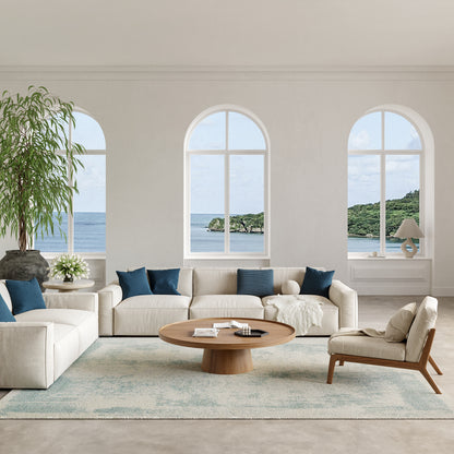 Bright coastal living room with cream sofas, blue cushions, round wooden coffee table, arched windows with ocean view.