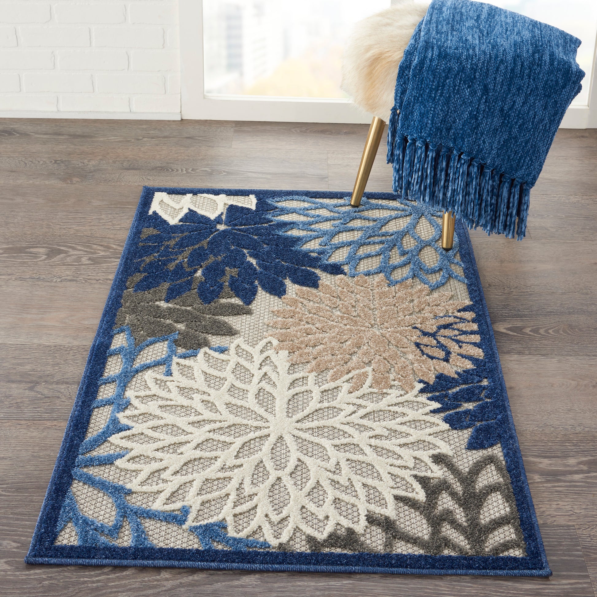 Rectangular woven area rug with large white floral motif and blue-tan leaves, blue border on wood floor.