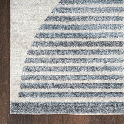 Blue striped area rug with curved horizontal bands on a light cream background, laid on dark wood floor.