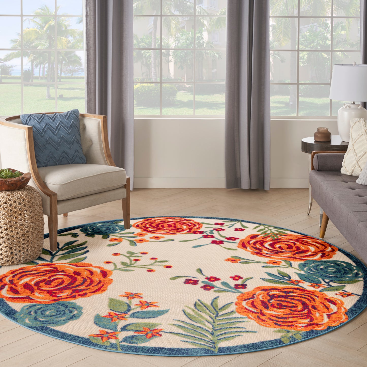 Round floral area rug with large orange roses, blue-green leaves, cream background, blue border, in a bright living room.