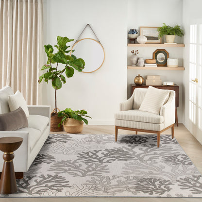 Neutral living room with striped beige armchair, light sofa, large potted plants, round wall mirror, and botanical rug.