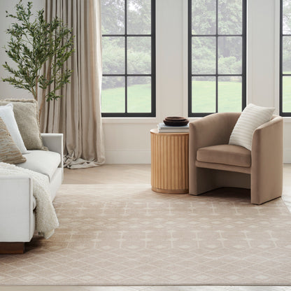 Neutral living room with beige fabric armchair, light sofa, round grooved wood side table, tall plant, and pale rug.