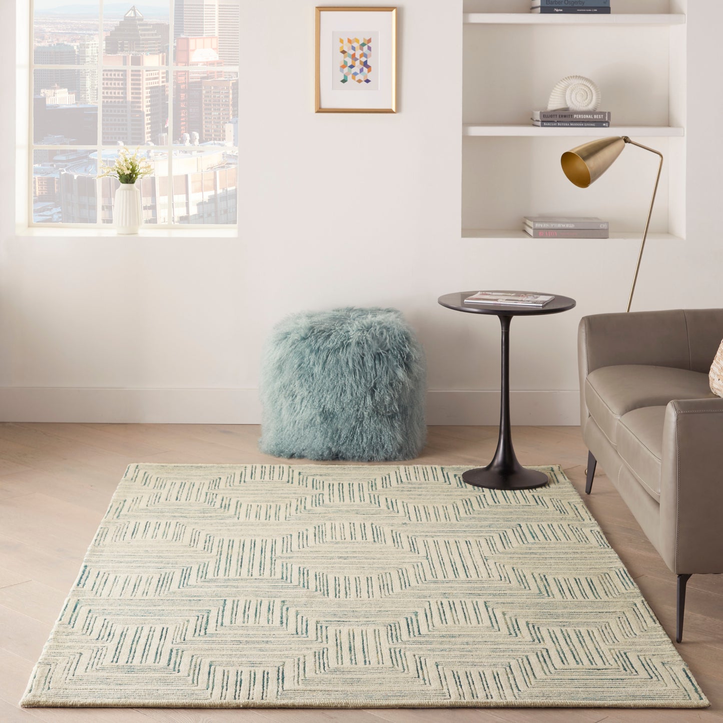 Cream geometric area rug with teal accents in a bright modern living room; fluffy blue pouf, black side table, gold lamp.