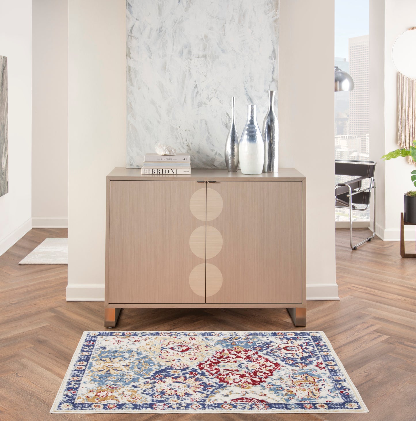 Light wood sideboard with three circular inlays, topped with silver vases and books, in a modern living room with a blue rug.