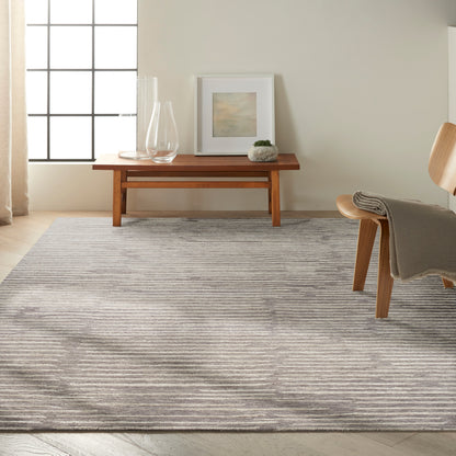 Light living room with a gray striped area rug, wooden coffee table, glass vases, framed art, and a wooden chair with a throw.