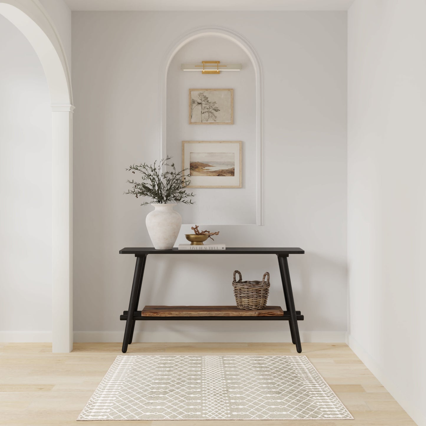 Dark wooden console with vase of greenery, wicker basket, and tray under framed art in a white arched alcove with rug