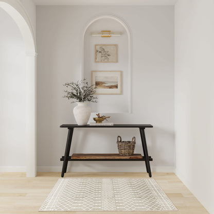Dark wooden console with vase of greenery, wicker basket, and tray under framed art in a white arched alcove with rug