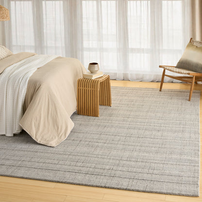 Neutral bedroom with beige duvet, light striped sheets, wooden side table, ceramic vase, woven chair, sheer curtains, rug.