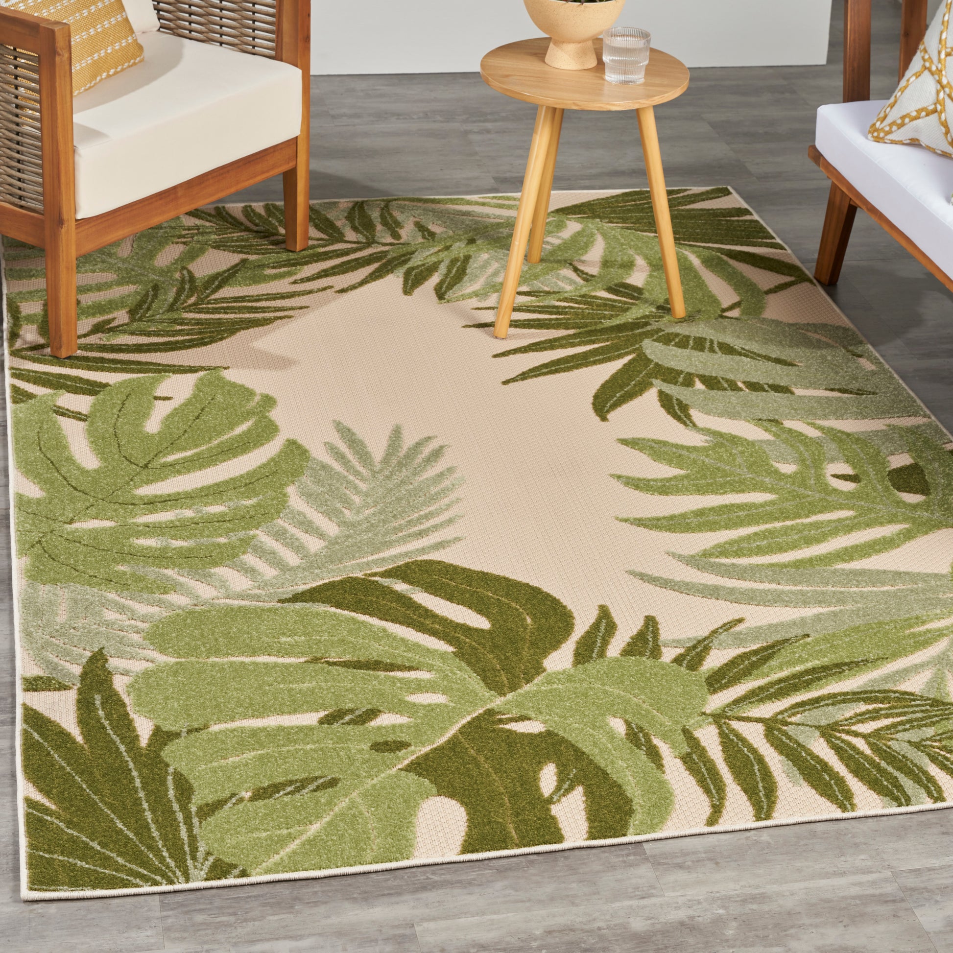 Beige outdoor rug with large green monstera and palm leaf pattern; outdoor wooden chairs & round table.