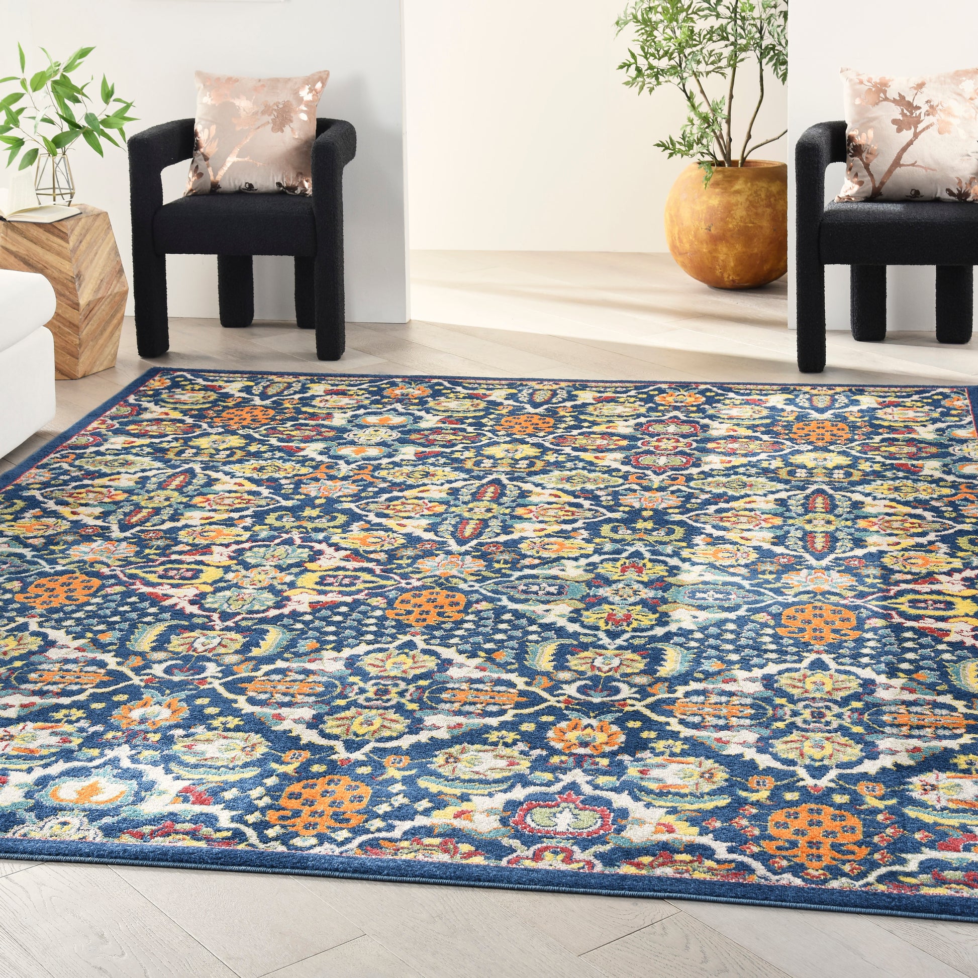 Vibrant navy oriental rug with orange, teal, and cream florals in a bright living room with black armchairs and potted plants.