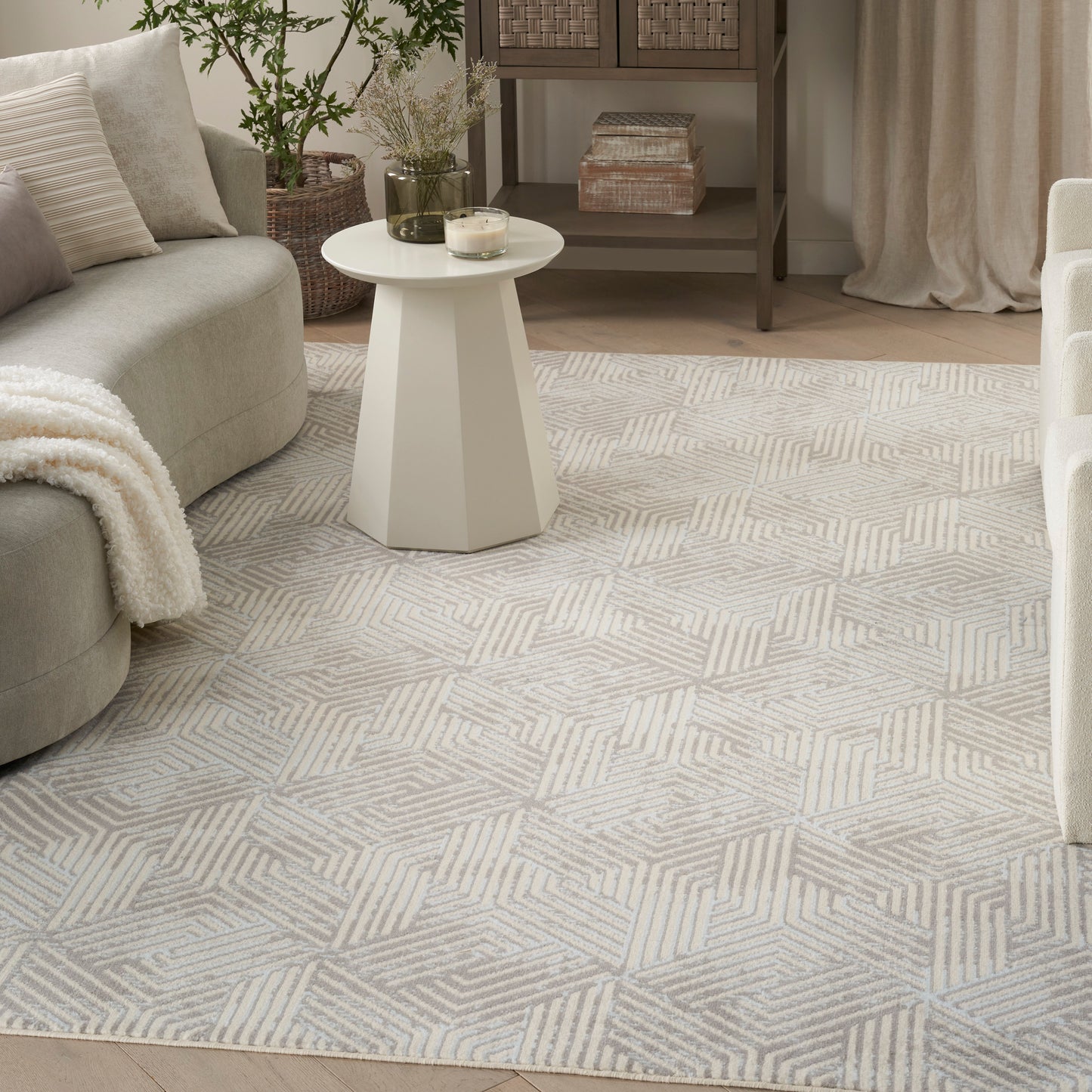 Geometric beige-gray area rug in a cozy living room with a round white pedestal table, gray sofa, and plants.