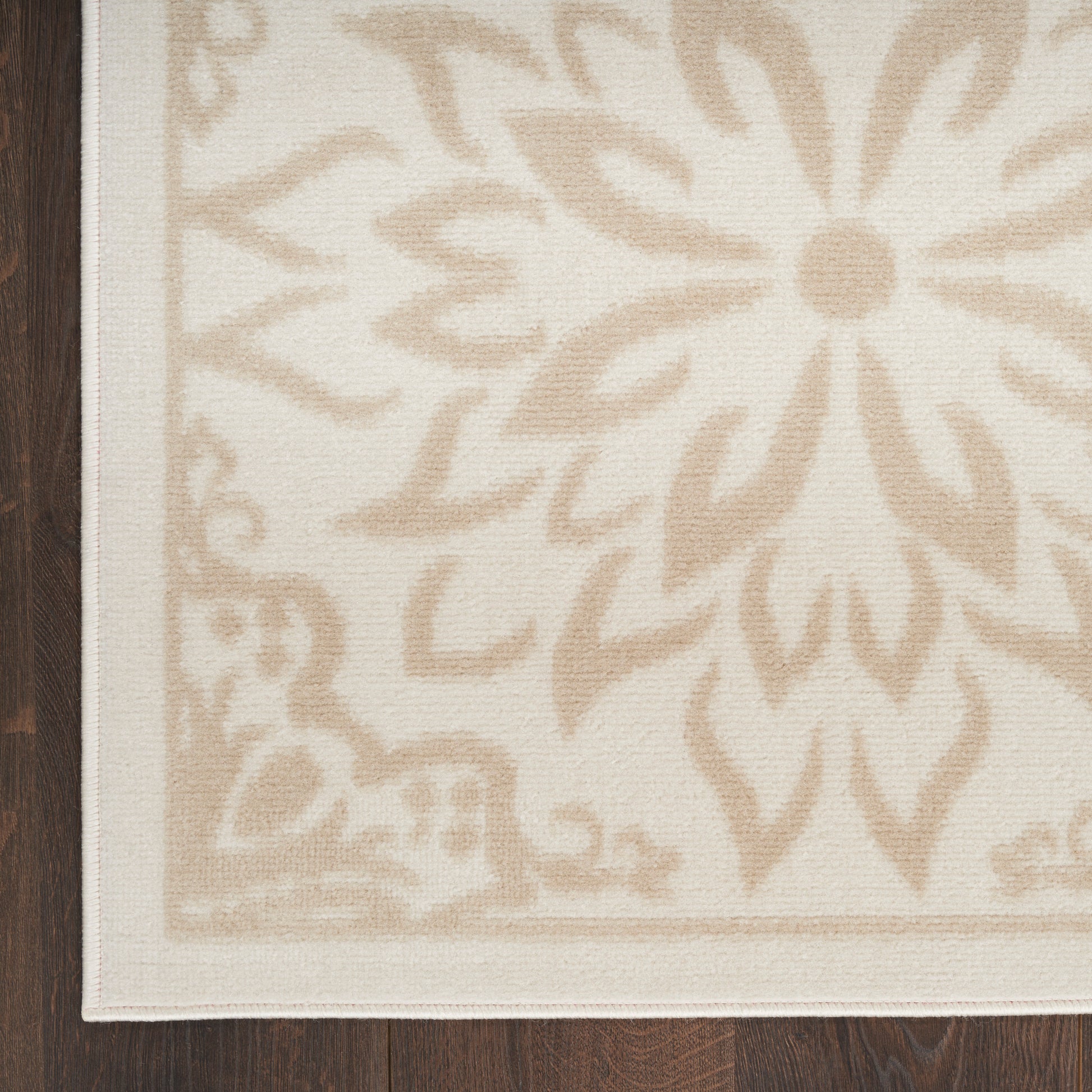 Cream-beige woven rug with large tan floral medallion pattern and bordered edge on dark wood floor.