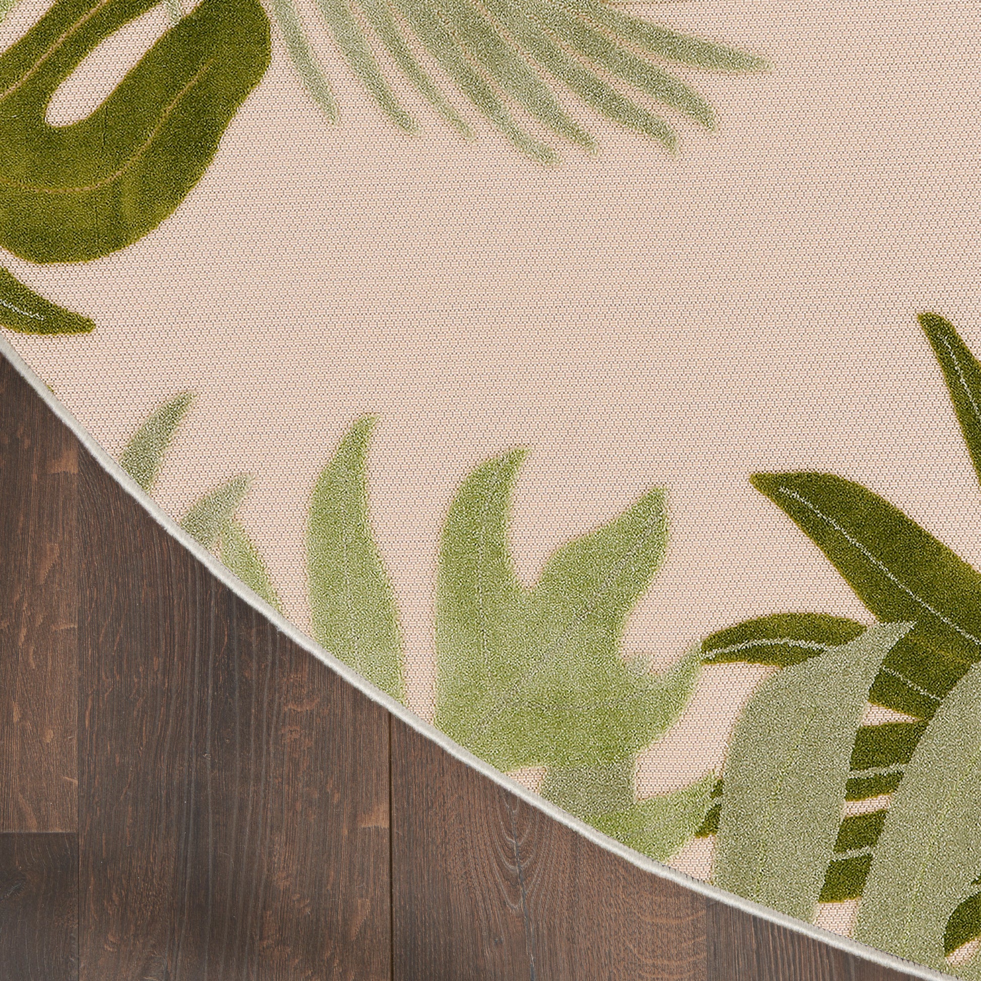 Round beige rug with green tropical leaf border design on dark wooden floor.