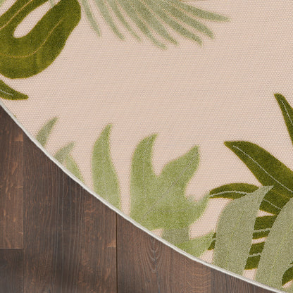 Round beige rug with green tropical leaf border design on dark wooden floor.