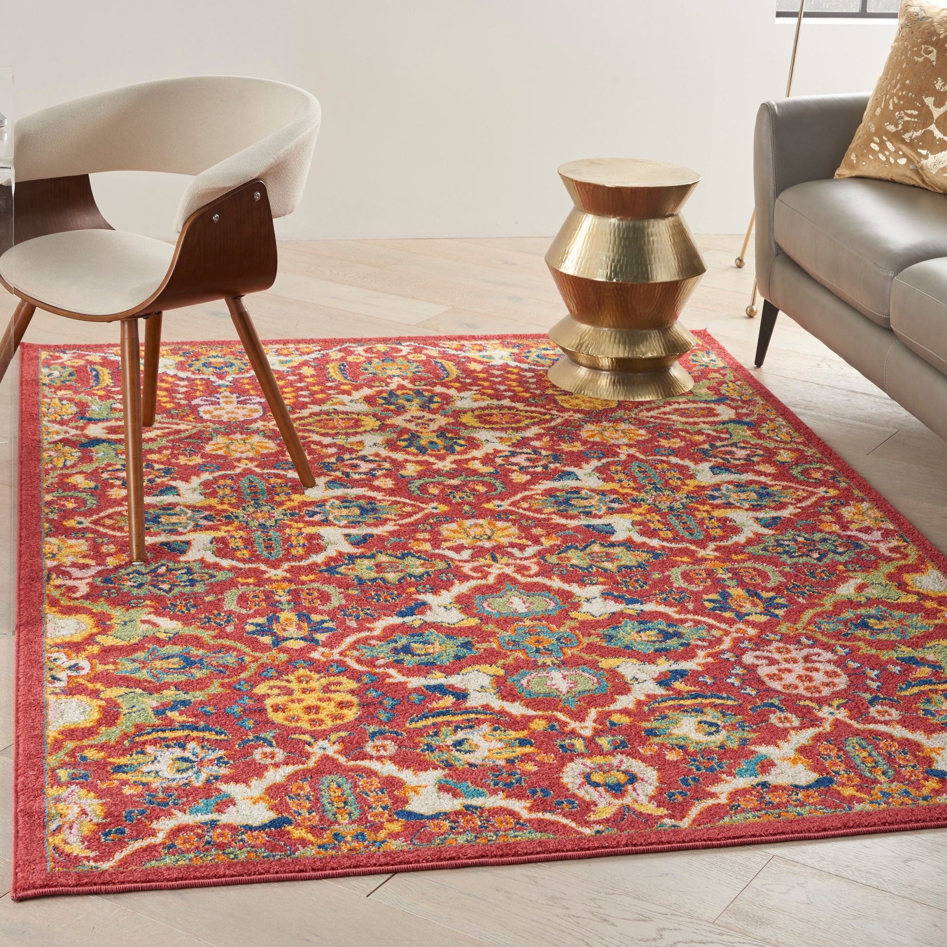 Colorful Bohemian rug in red, orange, blue, and yellow with a mid-century chair and gold stacked side table beside a gray sofa.