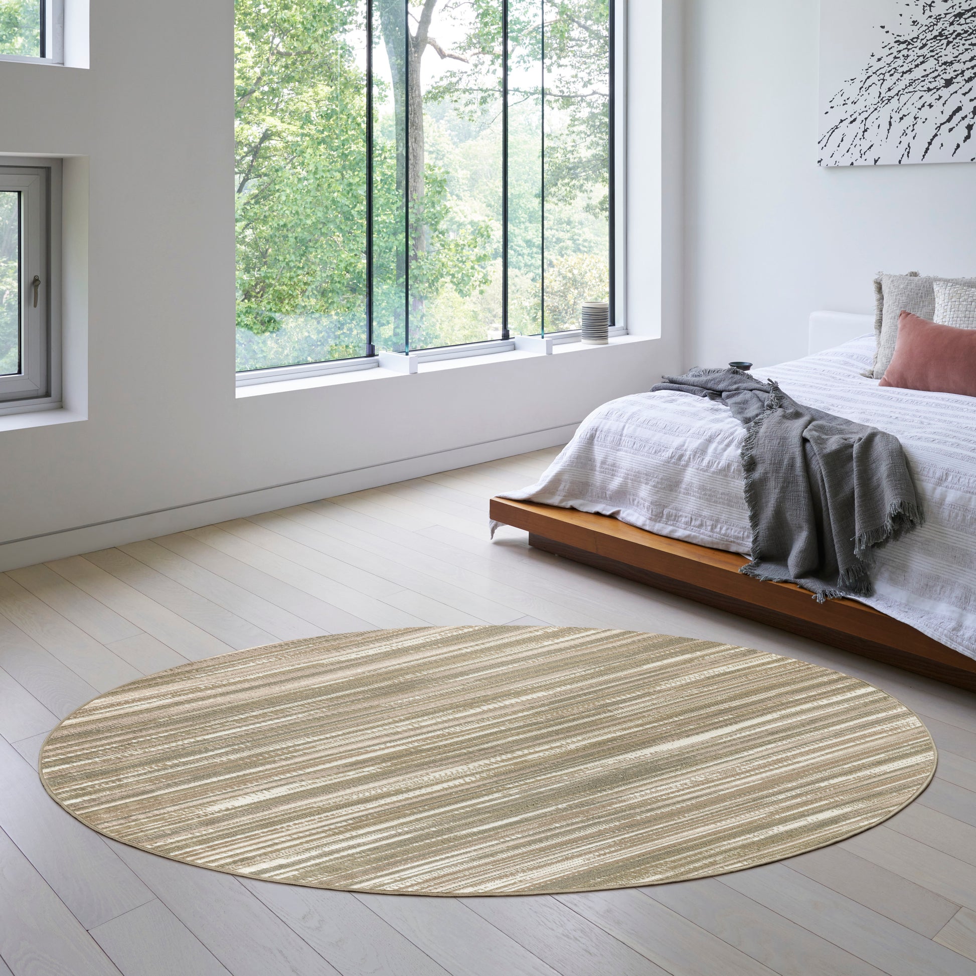 Round beige striped circular rug on light wood floor in an airy modern bedroom with a low platform bed and white linens.