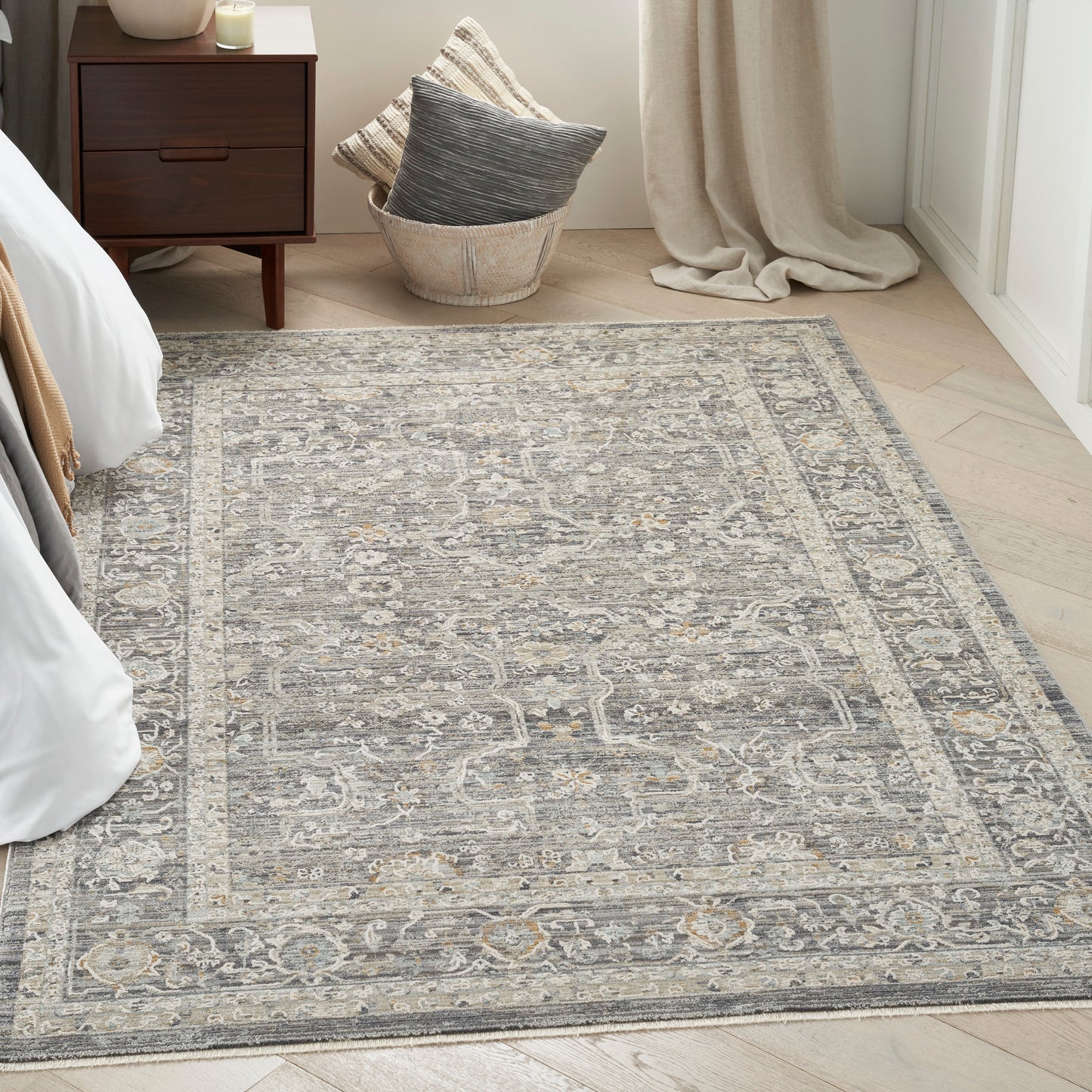 Grey and ivory vintage-style oriental area rug with an ornate border in a bright bedroom beside a dark wood nightstand.