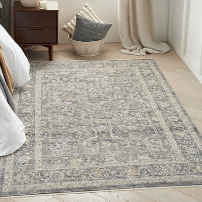 Grey and ivory vintage-style oriental area rug with an ornate border in a bright bedroom beside a dark wood nightstand.