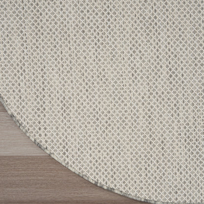 Round beige woven rug with subtle grey lattice pattern and fringed edge on light wood floor.