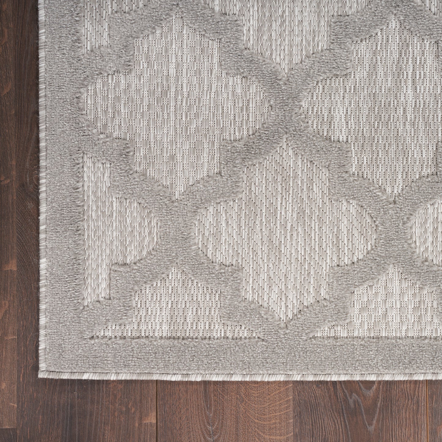 Light gray area rug with a geometric lattice pattern and textured weave, bordered edge on dark wood floor.