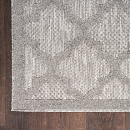 Light gray area rug with a geometric lattice pattern and textured weave, bordered edge on dark wood floor.