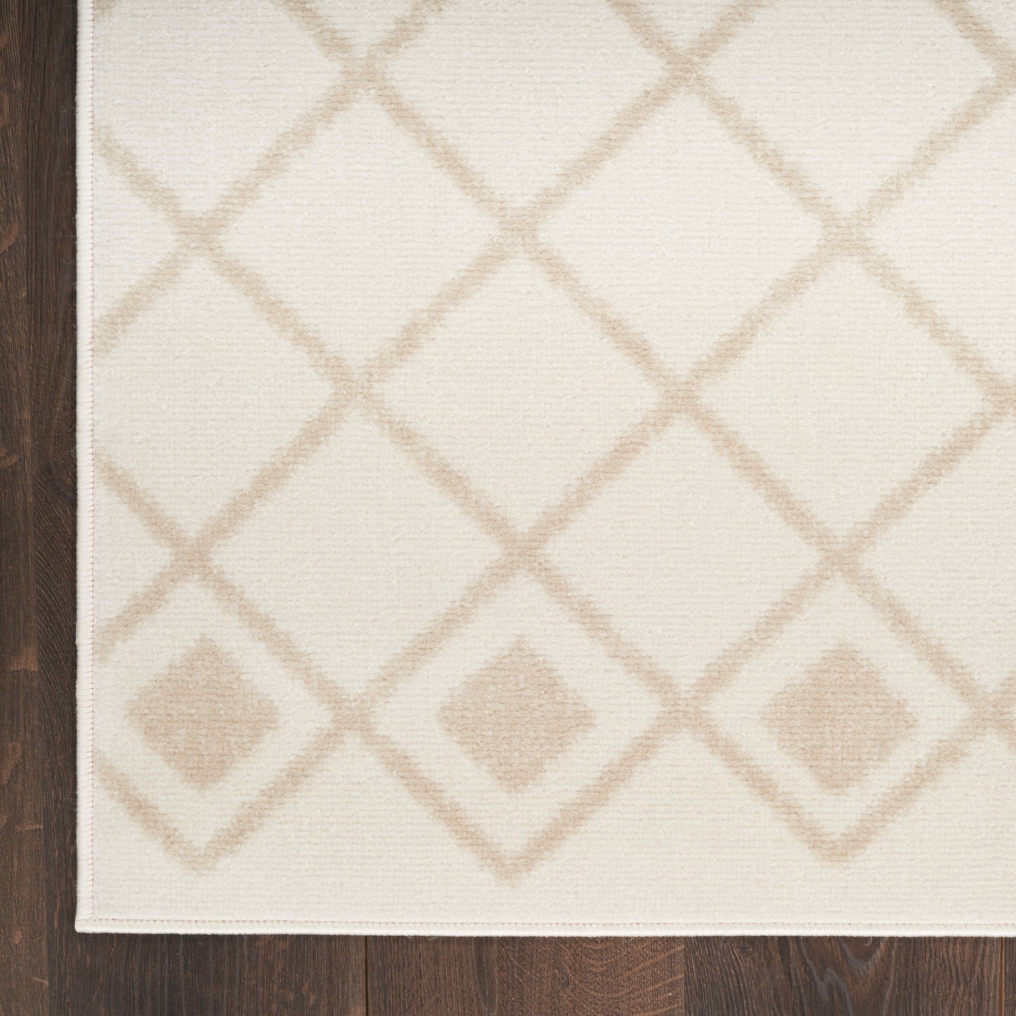 Cream flatweave rug with beige diamond lattice pattern on ivory background, placed on dark wood floor.