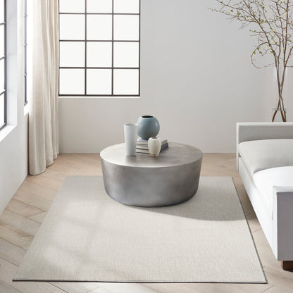 Minimalist living room with round concrete coffee table, neutral rug, white sofa, and decorative vases by a grid-window.