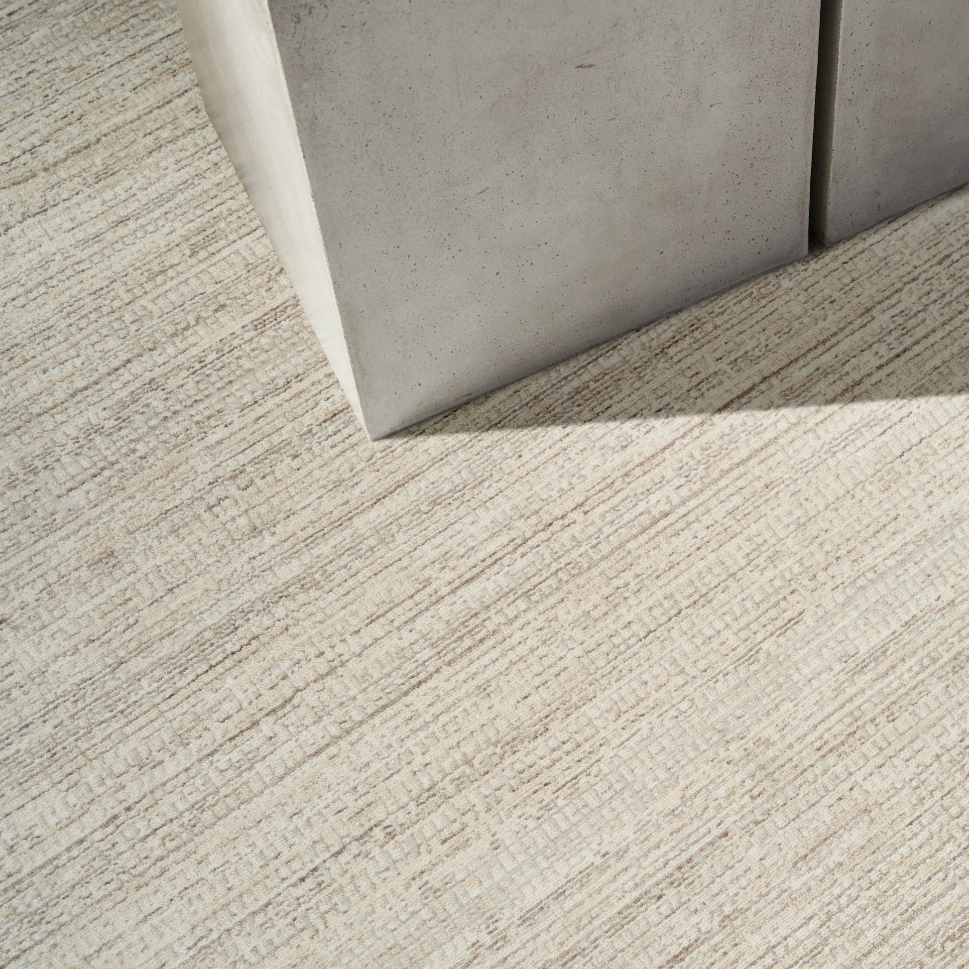 Beige textured carpet with a linear pattern beside a light gray concrete block edge; industrial modern interior detail.