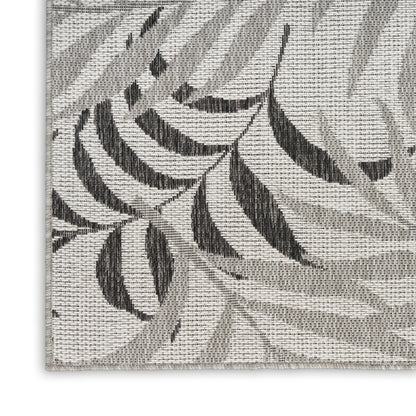 Close-up of a gray woven rug with charcoal leaf pattern, textured jacquard, and a border at the corner.