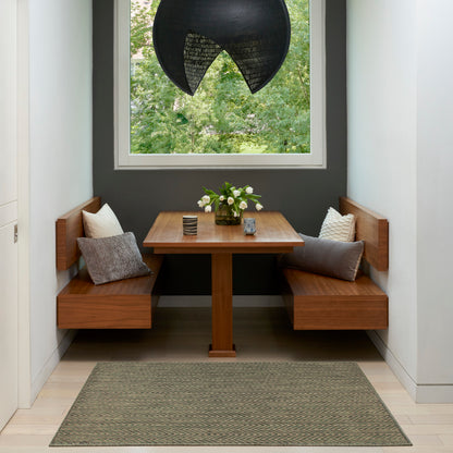 Built-in wooden booth dining nook with square table, gray walls, greenery outside window, black pendant light, cushions and vase of white flowers.