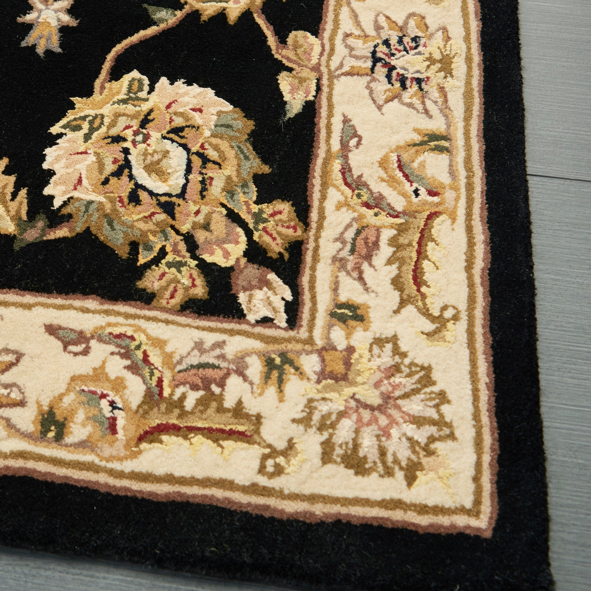 Traditional oriental rug with black field and cream/gold border, ivory floral scrolls; on wood floor.