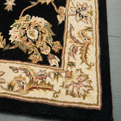 Traditional oriental rug with black field and cream/gold border, ivory floral scrolls; on wood floor.
