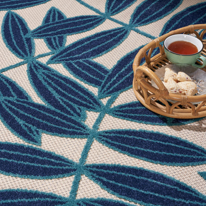 Blue leaf-patterned woven rug with beige background; wicker basket holding a green ceramic cup of tea and cookies.