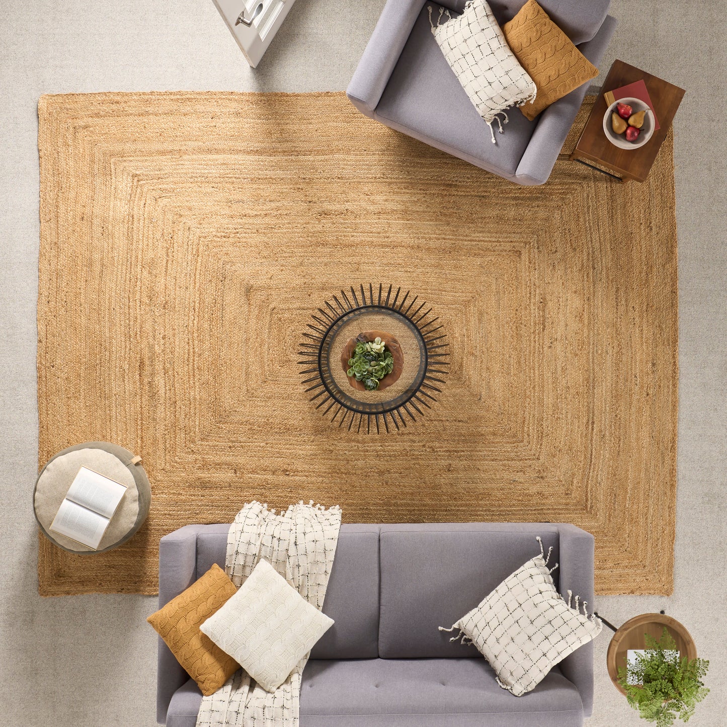 Overhead view of a living room with a large jute rug, gray sofa, mustard and cream pillows, and a sunburst centerpiece.