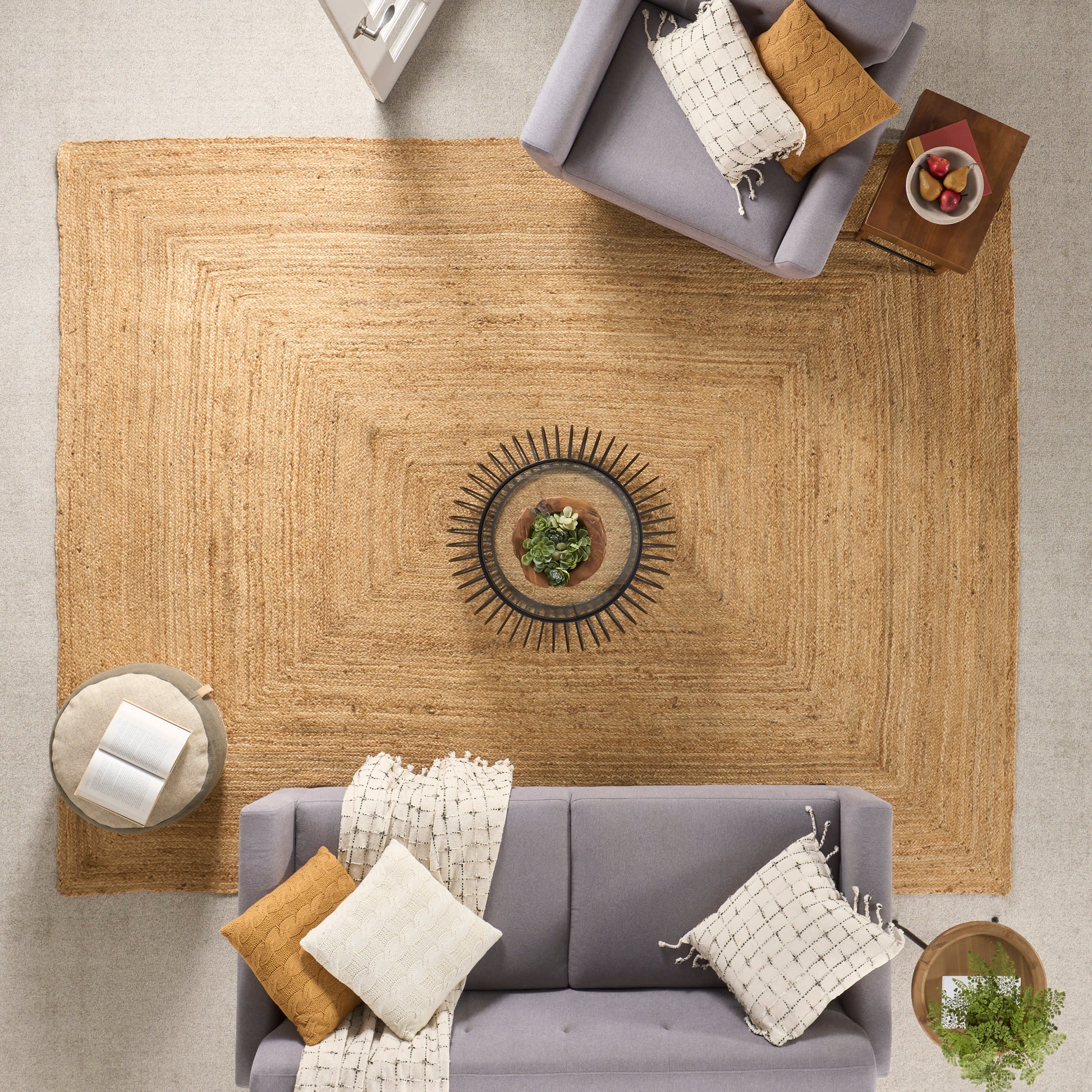 Overhead view of a living room with a large jute rug, gray sofa, mustard and cream pillows, and a sunburst centerpiece.