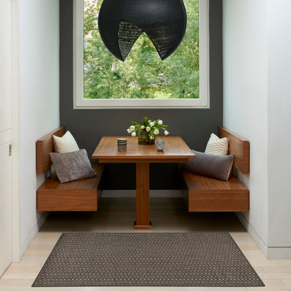 Warm wooden built-in dining nook with square table, grey cushions, and a chevron rug under a vase of white flowers.