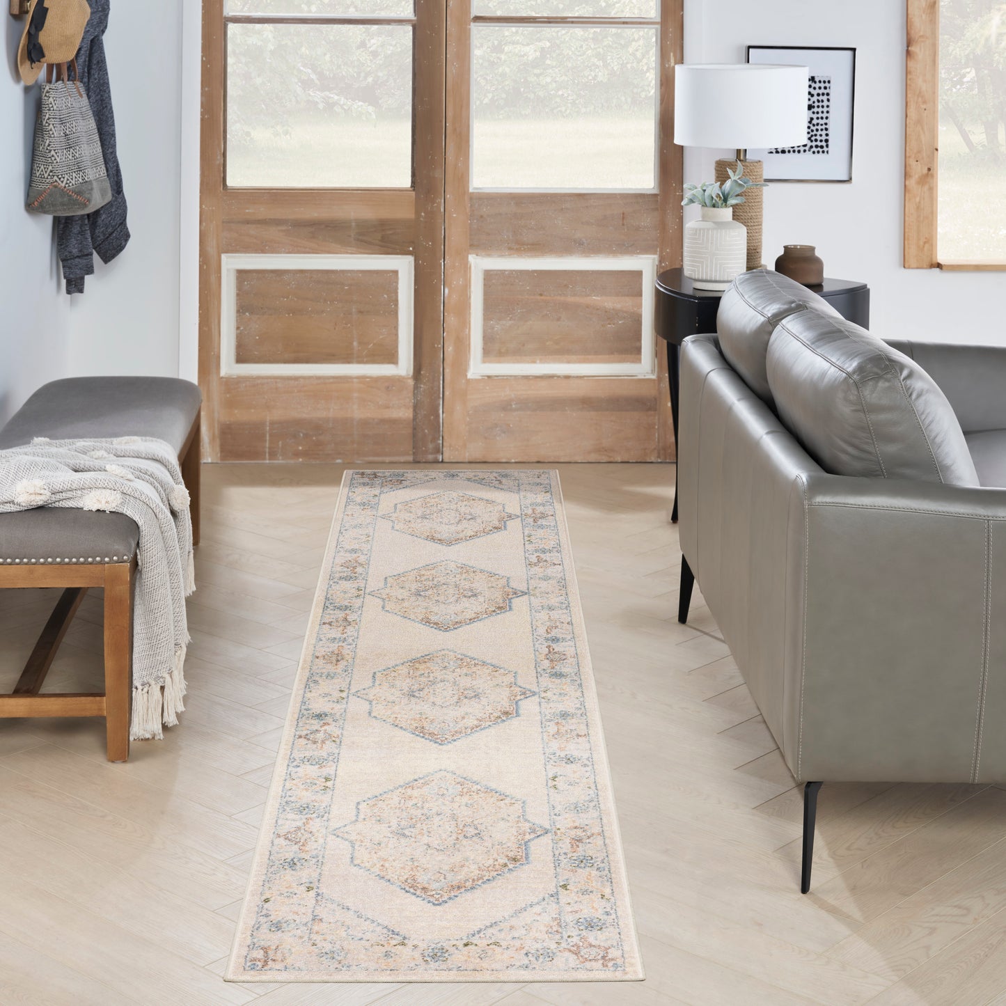 Entryway with wooden double doors, gray leather sofa, bench with throw, and a beige-blue diamond-pattern runner rug.
