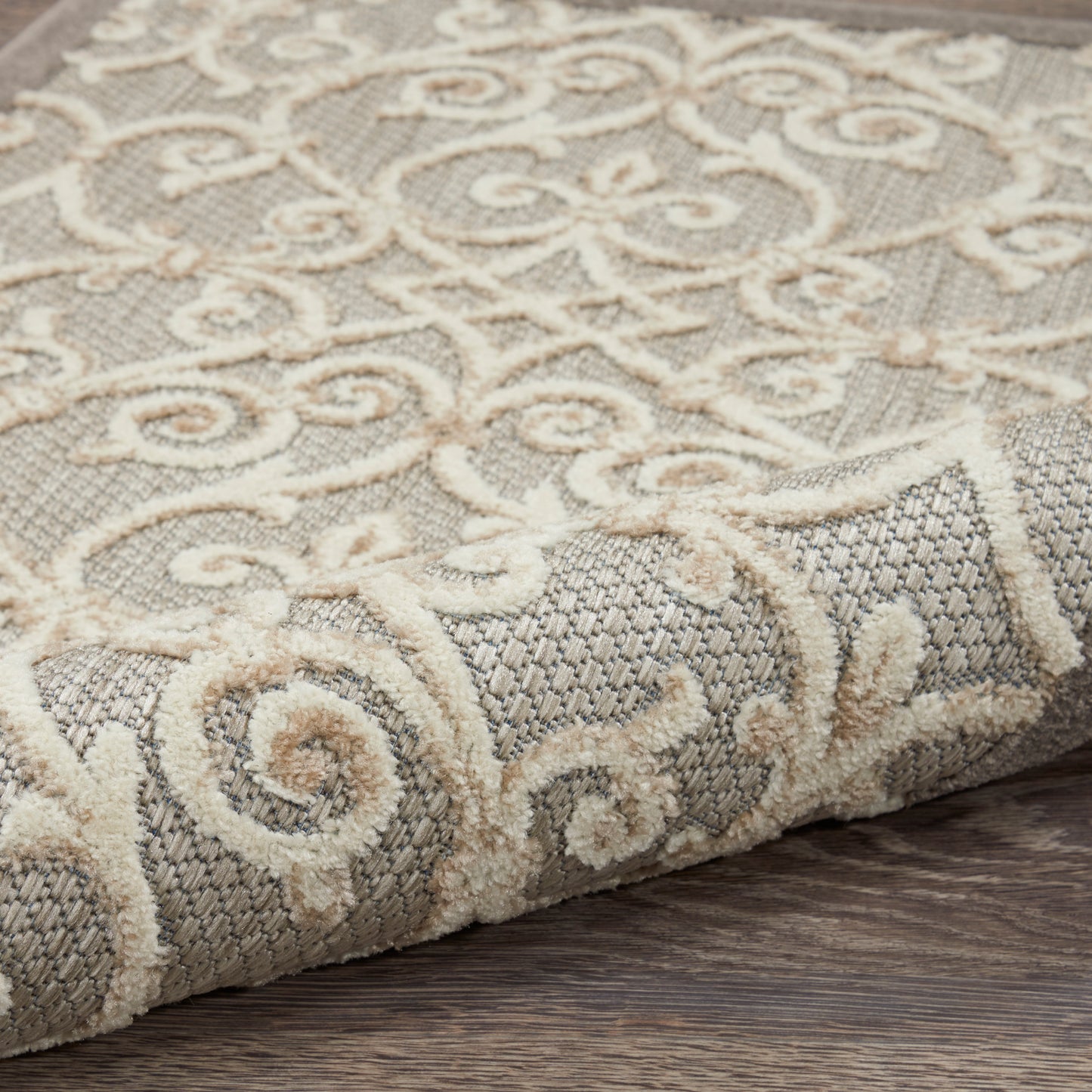 Ornate cream-scroll patterned rug with gray woven backdrop, rolled edge on wood floor.