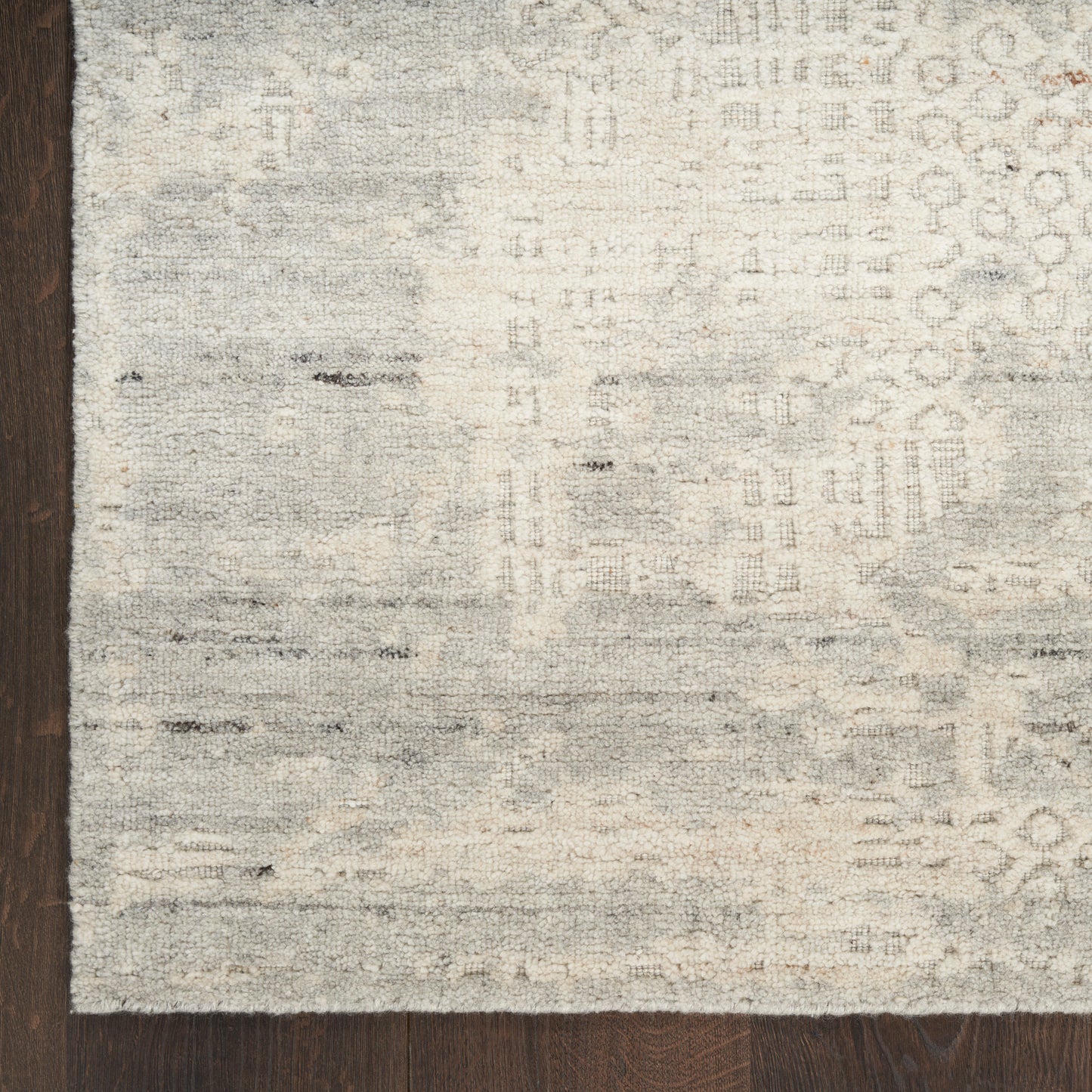 Muted light gray-beige area rug with abstract pattern on dark wood floor.