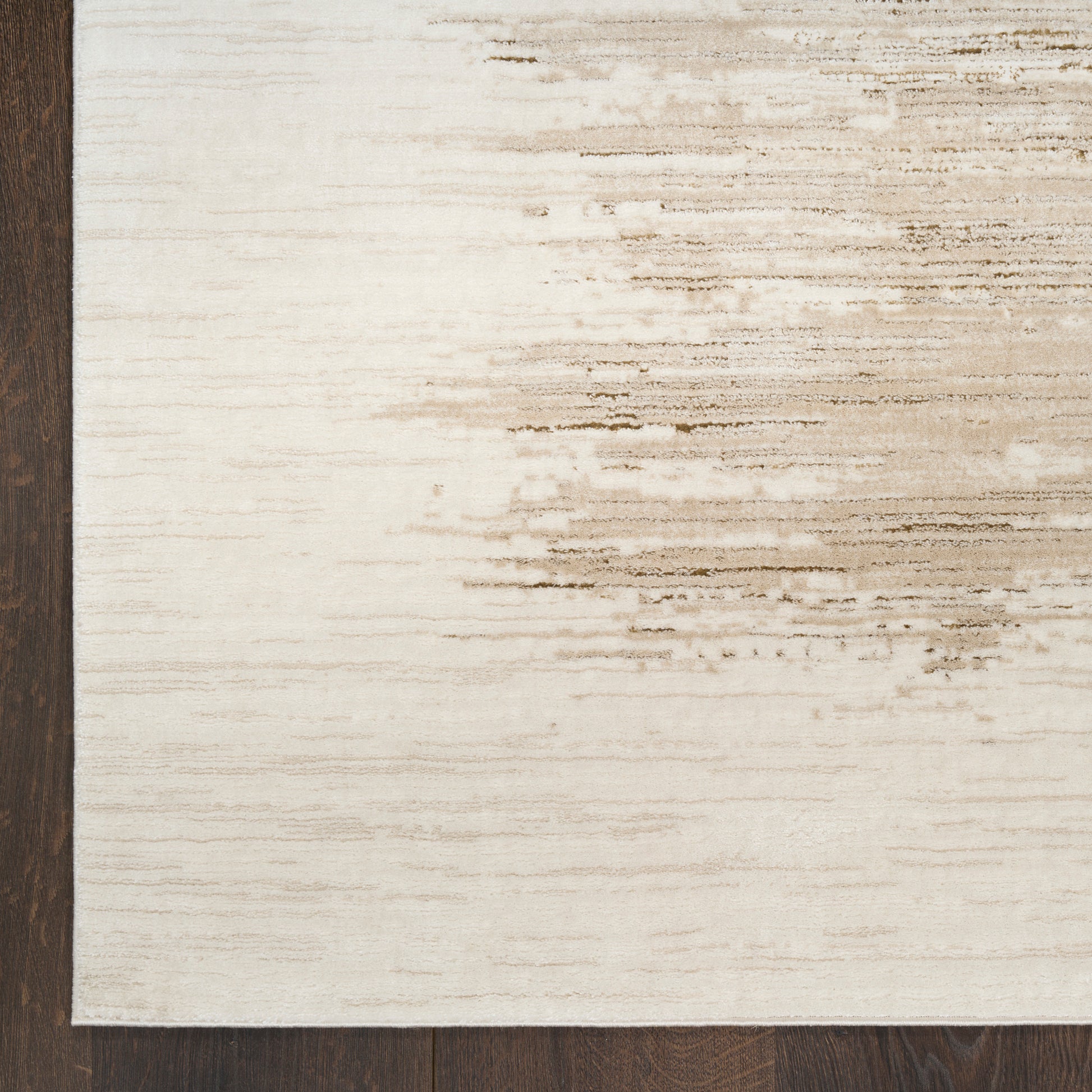Cream area rug with tan brushstroke pattern on the right, dark border along the left edge on a wood floor.