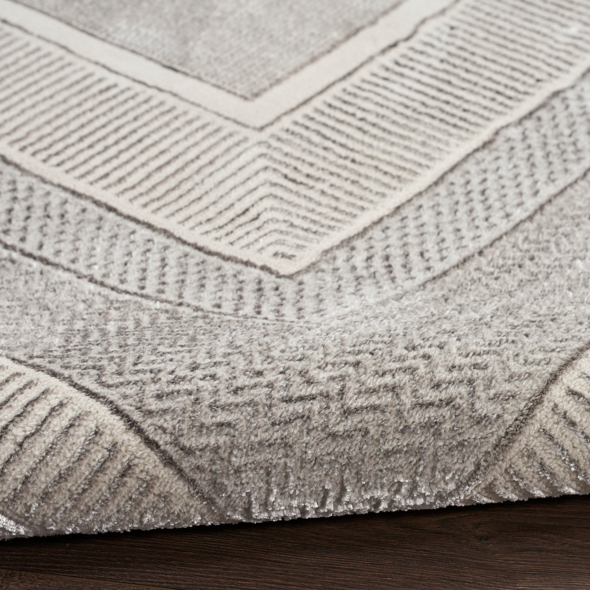 Close-up of a light gray geometric rug with textured chevron pattern and border on dark wood floor.