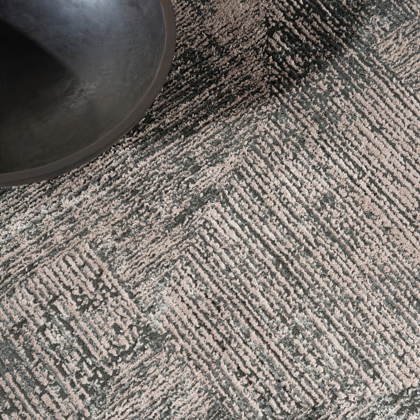Dark matte metal pet bowl resting on a gray geometric patterned rug.