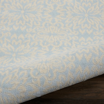 Light blue damask-patterned rug runner with cream motifs, folded along the edge on a dark wood surface