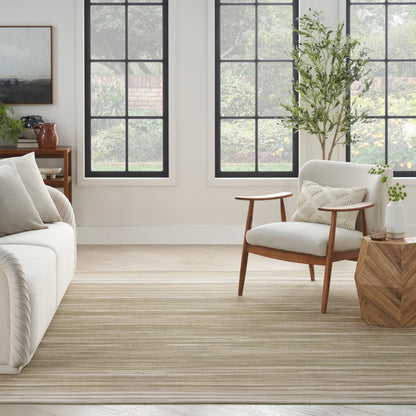 Bright living room with large windows, cream sofa, wood chair, striped beige rug, wooden side table, potted plant.