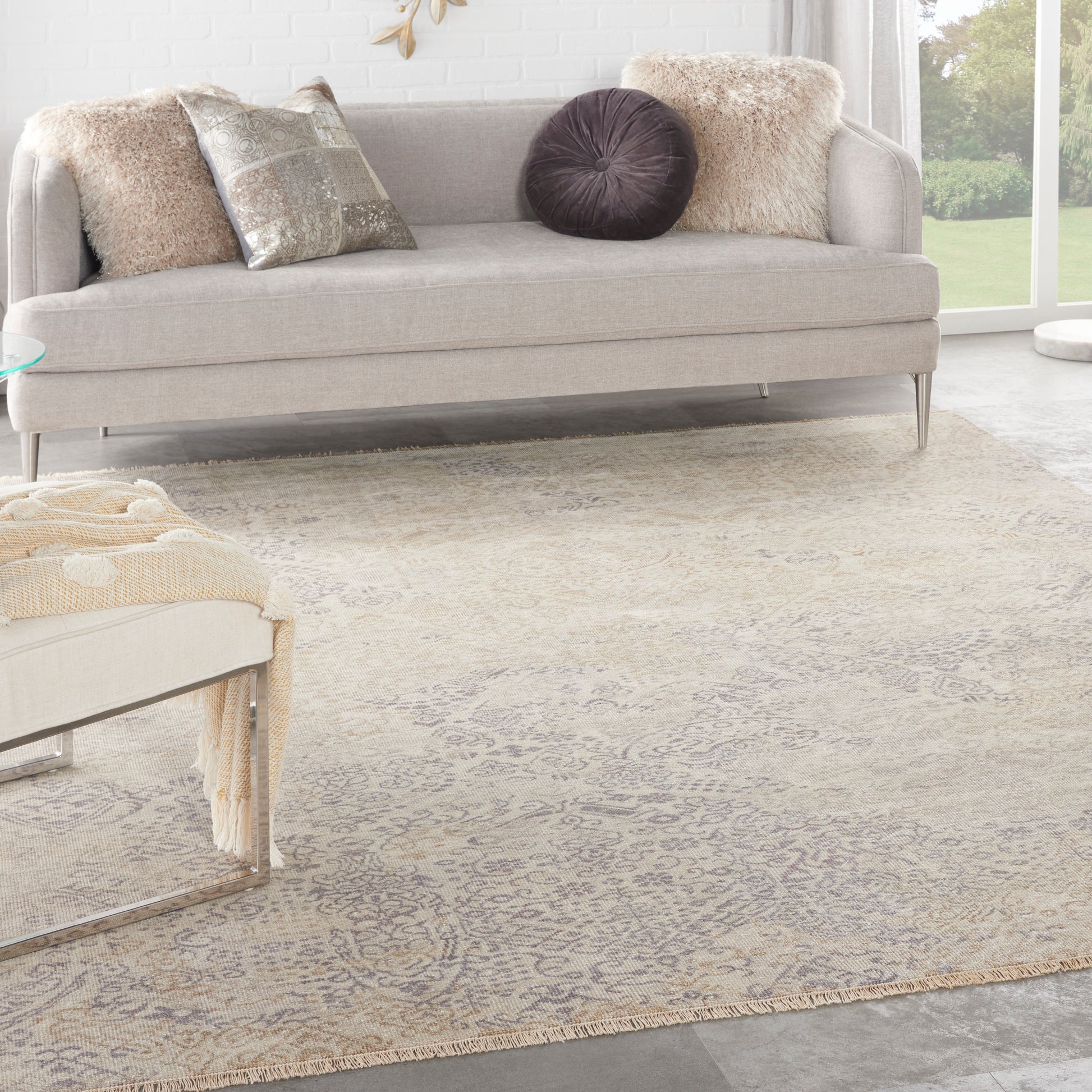 Beige patterned area rug on a bright contemporary living room floor, with a light gray sofa and metallic pillows nearby.