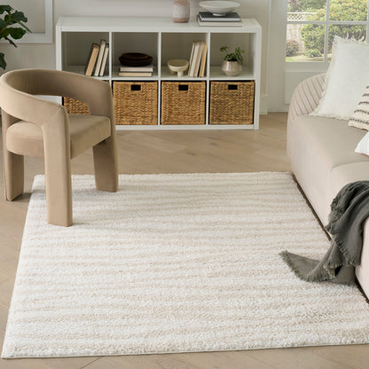 Cream plush shag area rug with subtle stripes, paired with a beige curved lounge chair and white cubby storage.