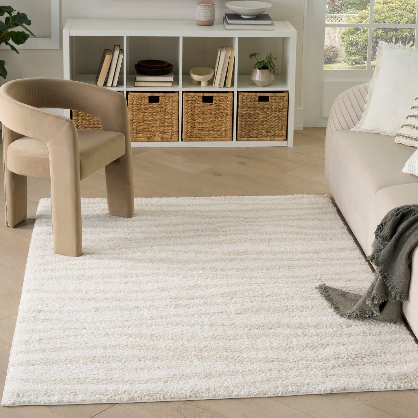 Beige curved accent chair, cream shag rug, white cubby storage & wicker baskets in a bright modern living room.