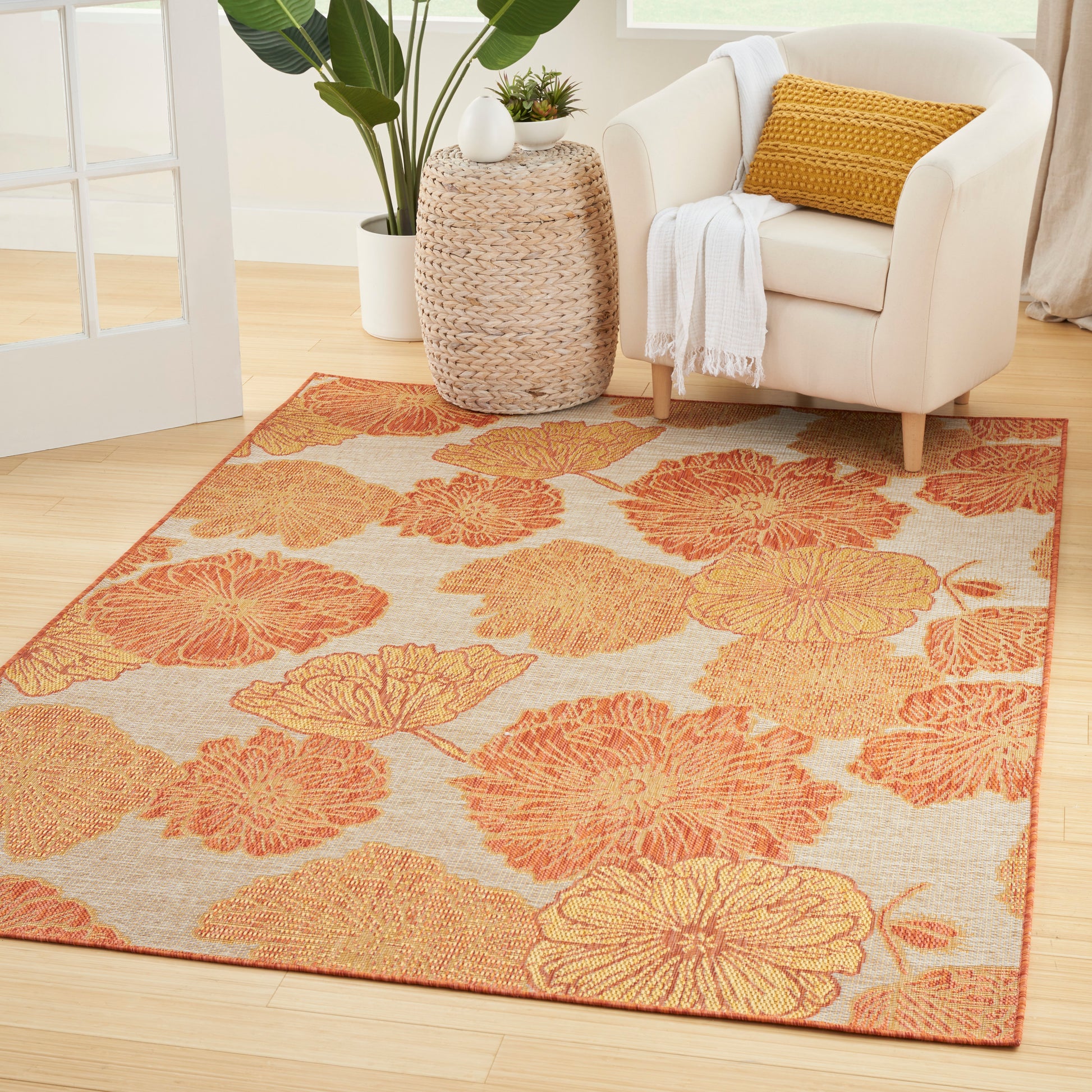 Beige rug with large orange floral pattern in a bright living room with a cream armchair and woven side table.